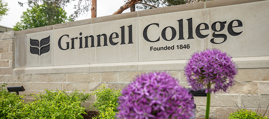 A stone Grinnell College sign welcomes you to campus and features purple flowers in the foreground