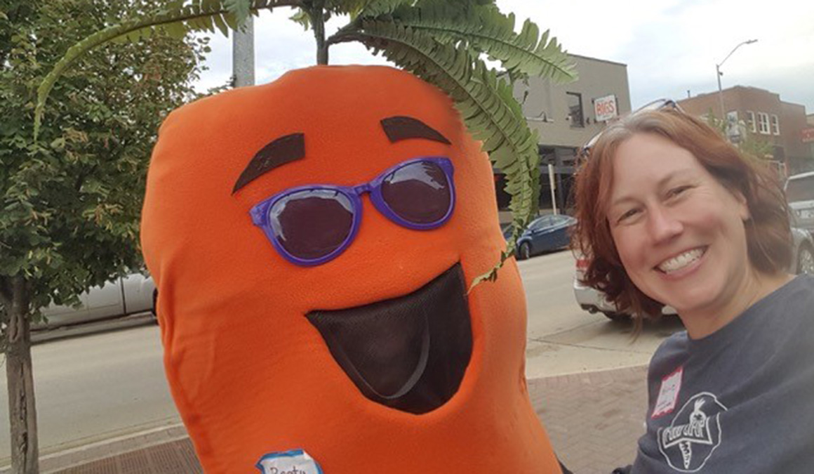 Melanie Drake ’92 is pictured next to Rooty the Carrot, the mascot for the Rooted Carrot Co-op Market.